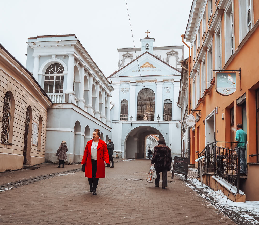 Woman in a red coat walking at the gates of dawn in vilnius lithuania