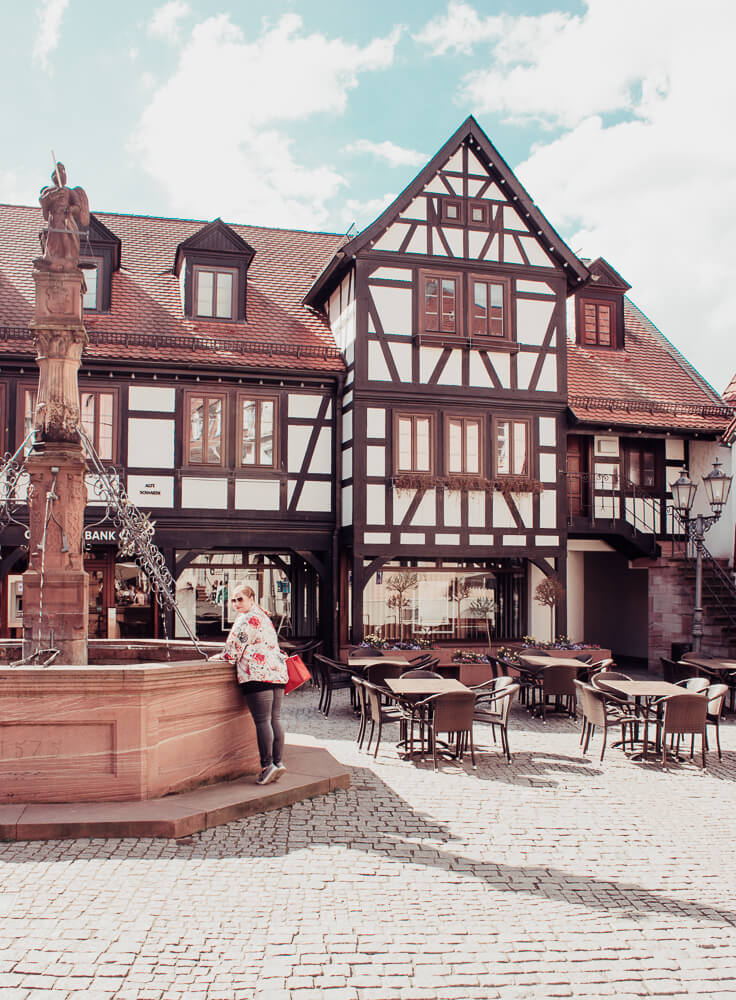 Woman looking at the ornate fountain, marktbrunnen, in the centre of Michelstadt town square