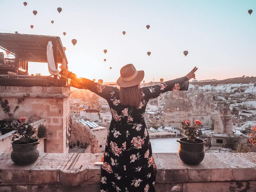 Woman in straw hat watching the hot air balloons during sunrise at the Kelebek special cave hotel in Cappadocia, Turkey. 