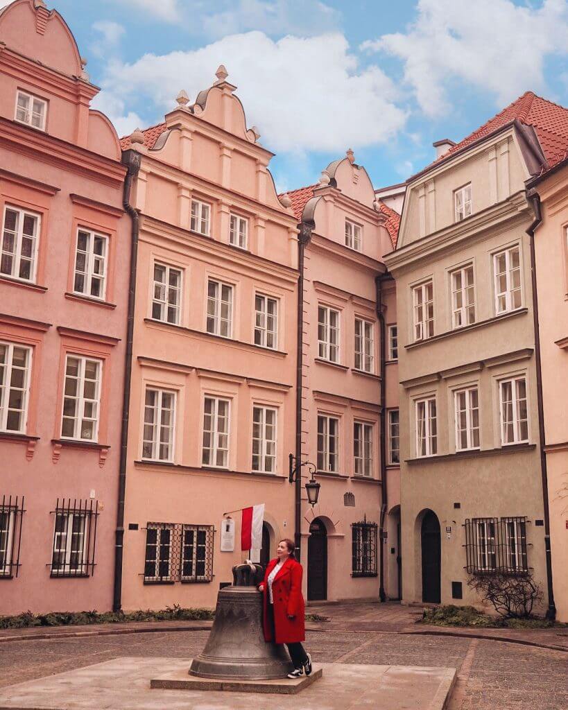Woman in a red coat looking up at the pastel buildings in Warsaw's alleyways. A pretty Instagram spot in Warsaw
