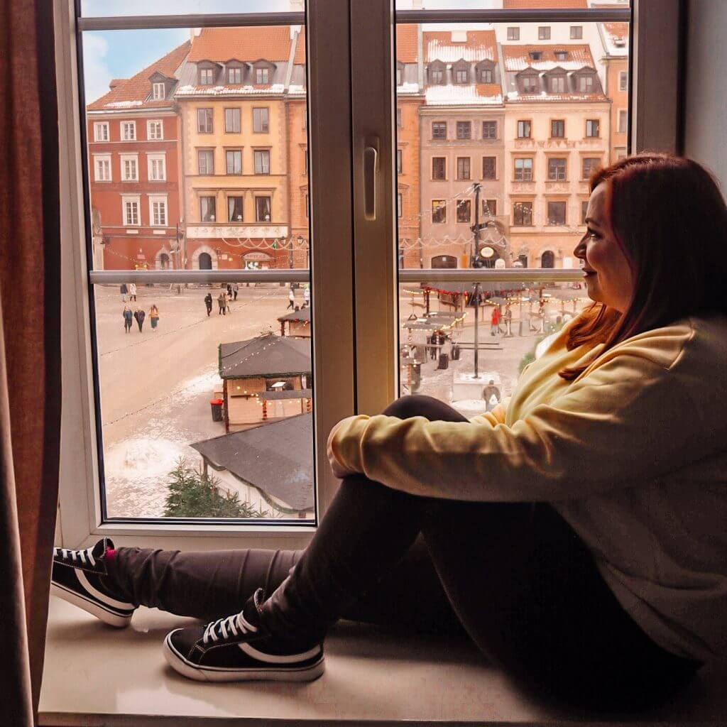 Woman sitting on a windowsill looking out at Warsaw Old town square at Christmas.