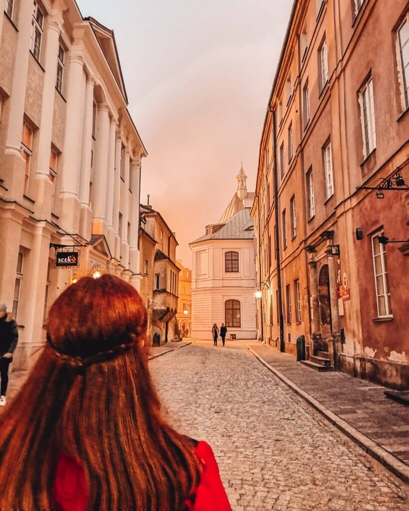 Woman with red hair looking down the cobbled streets of Warsaw at dusk