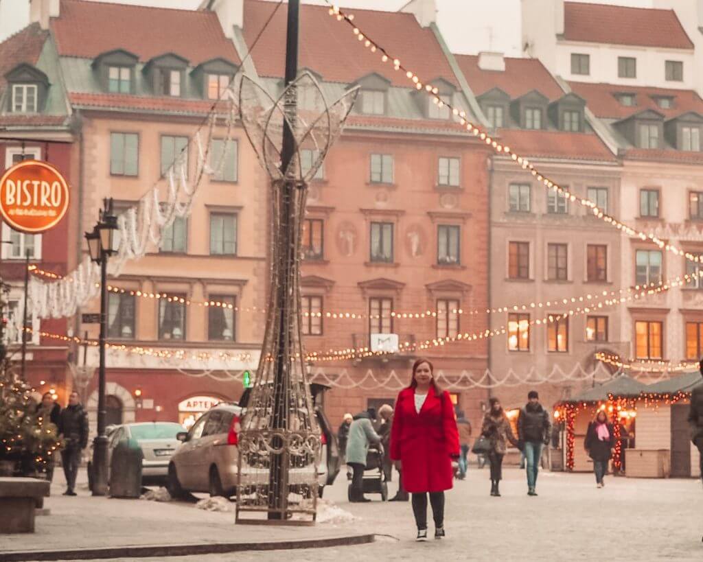 Woman in a red coat walking through Warsaw's old town square at Christmas