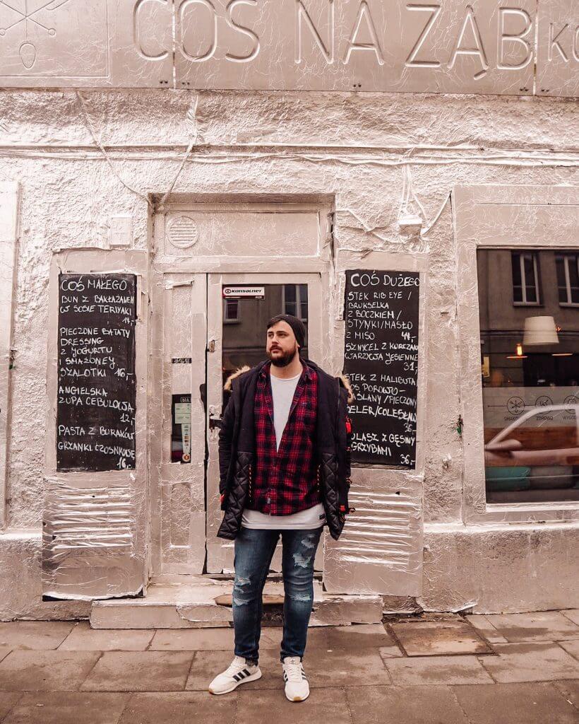 Man in a checked shirt standing in front of a building covered in tinfoil in Praga Warsaw