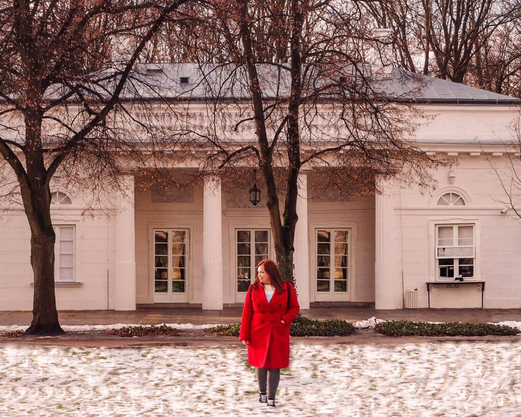 Woman in a red coat walking in the snow in a park in Warsaw