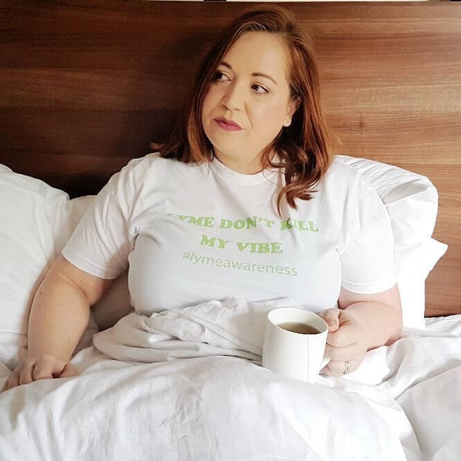 A woman with Lyme Disease lying in bed and drinking a herbal tea