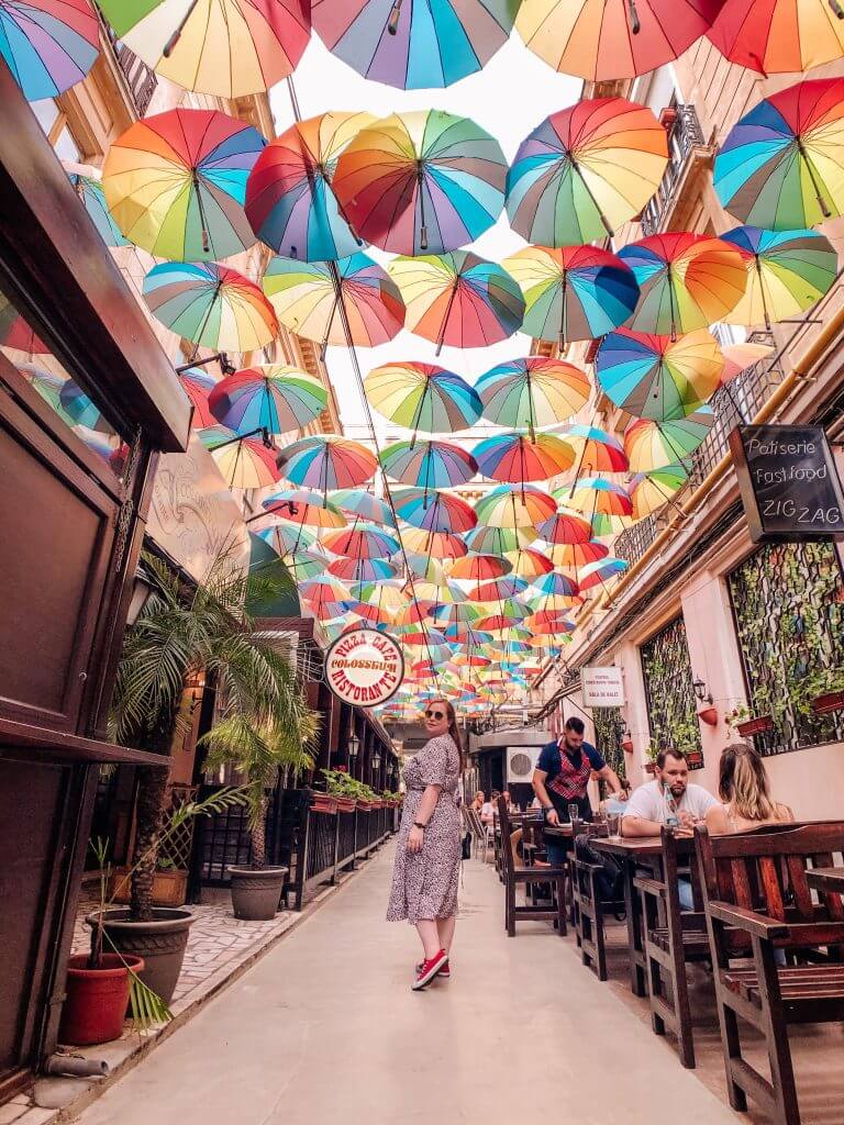 Woman standing under a colourful Umbrella sky in Bucharest. The best travel hashtags to use for killer reach. A list of over 250 travel hashtags for Instagram. Read more on www.allaboutrosalilla.com