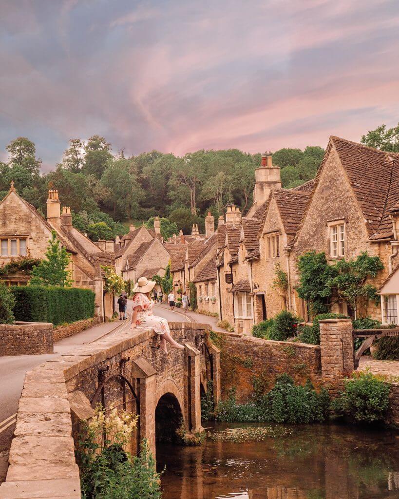 Woman sitting on the bridge in Castle Combe a village you must visit in the Cotswolds