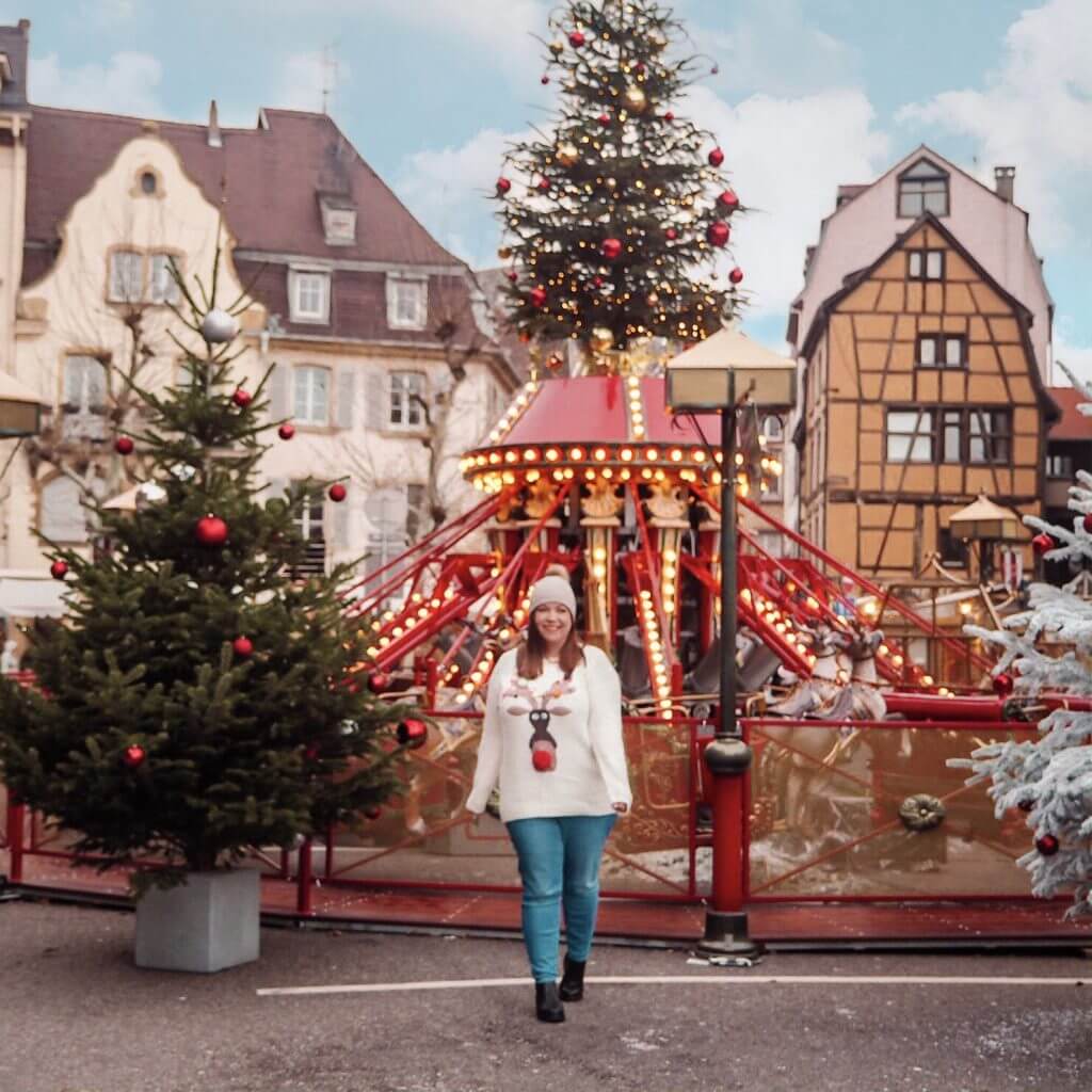 Woman wearing a Christmas jumper in front of a carousel in Colmar Alsace France