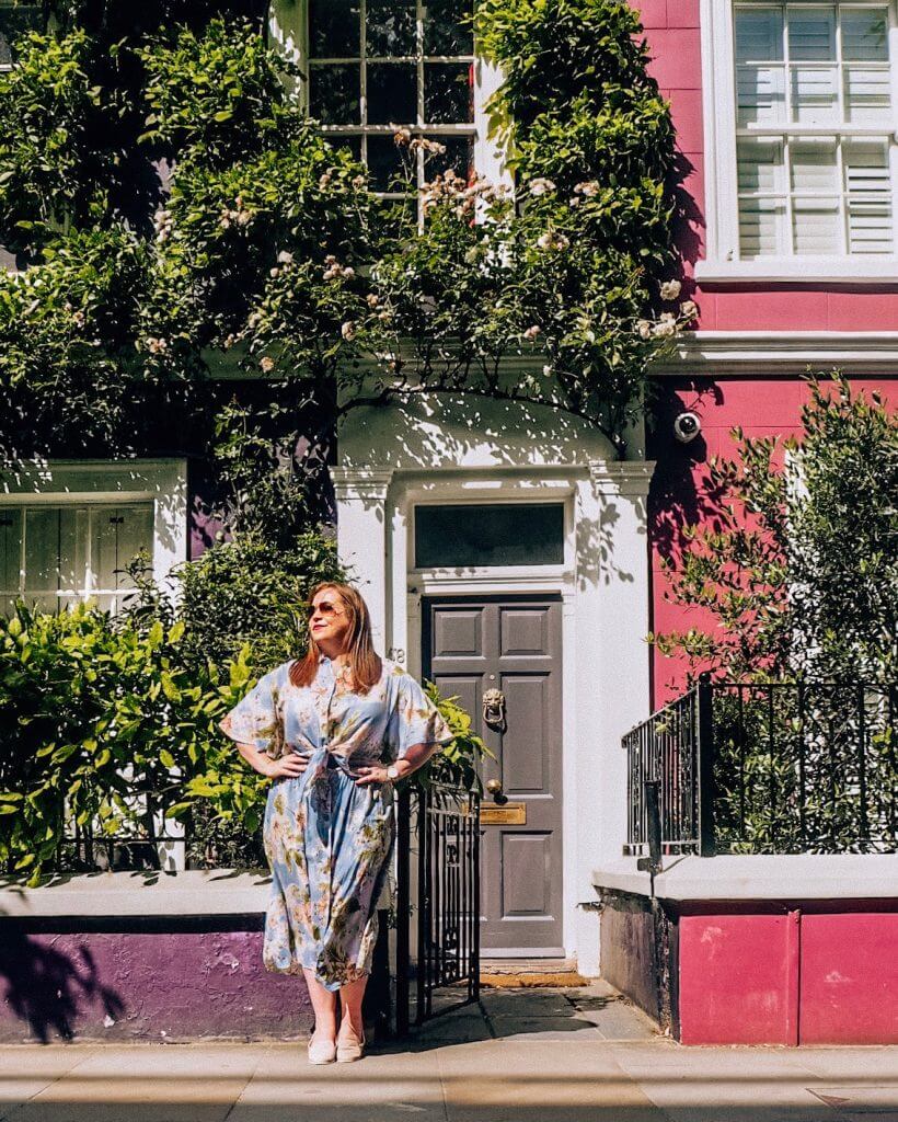 Woman in a blue floral dress posing in front of the pastel coloured houses of Notting Hill London