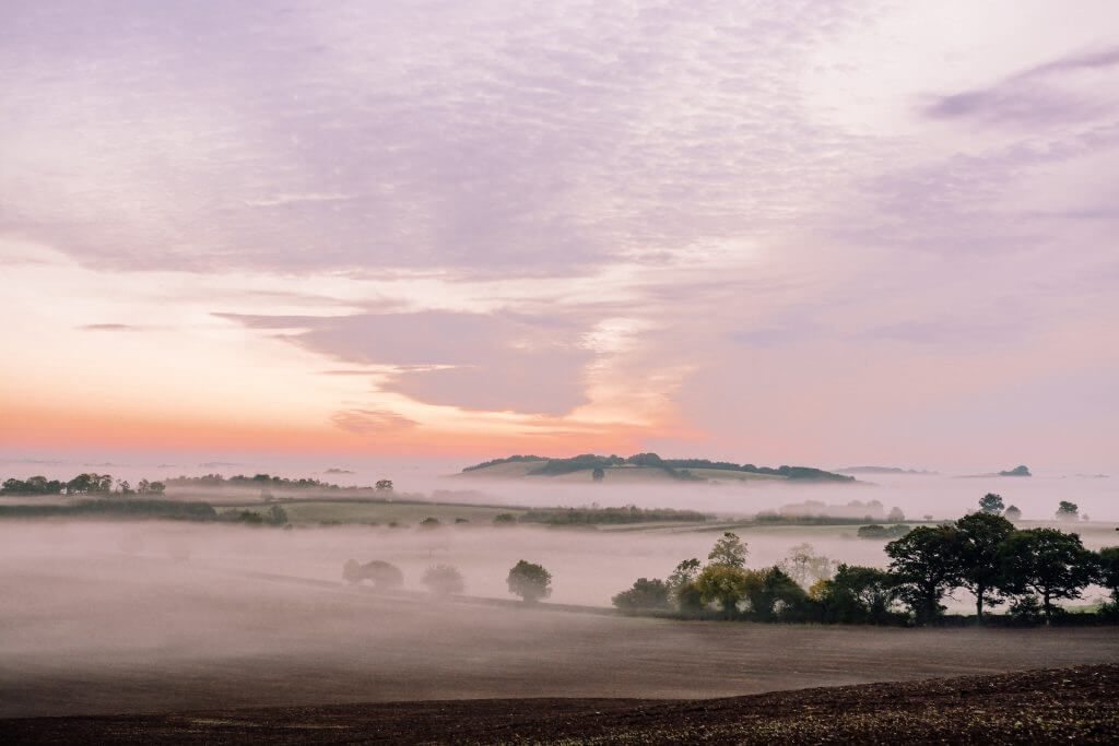 Picturesque view of rolling hills and meadows in the Cotswolds. Fog over the Cotswolds Countryside