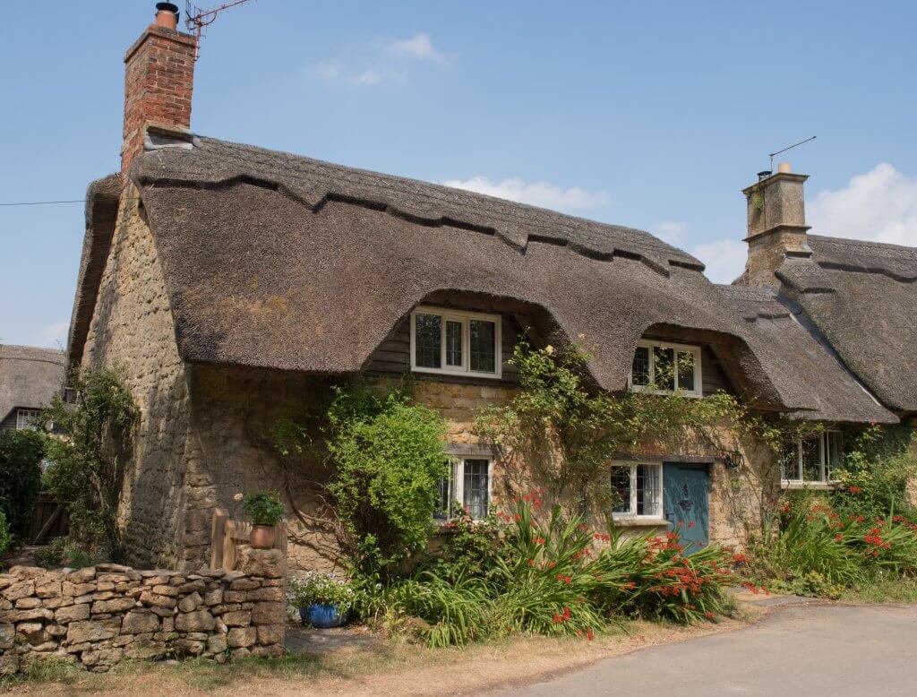 Quaint thatched-roof cottage framed by colourful flowers in the Cotswolds.