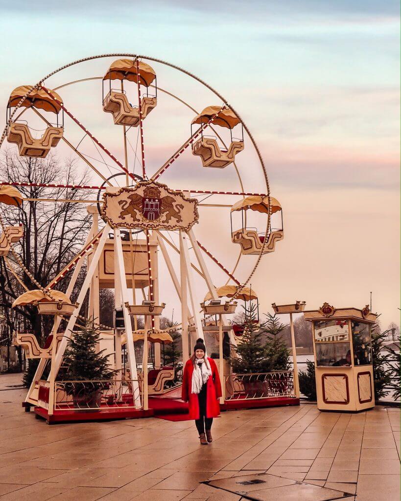 Girl in red coat standing in front of a ferris wheel at White magic by the Jungfernstieg Hamburg Christmas markets
