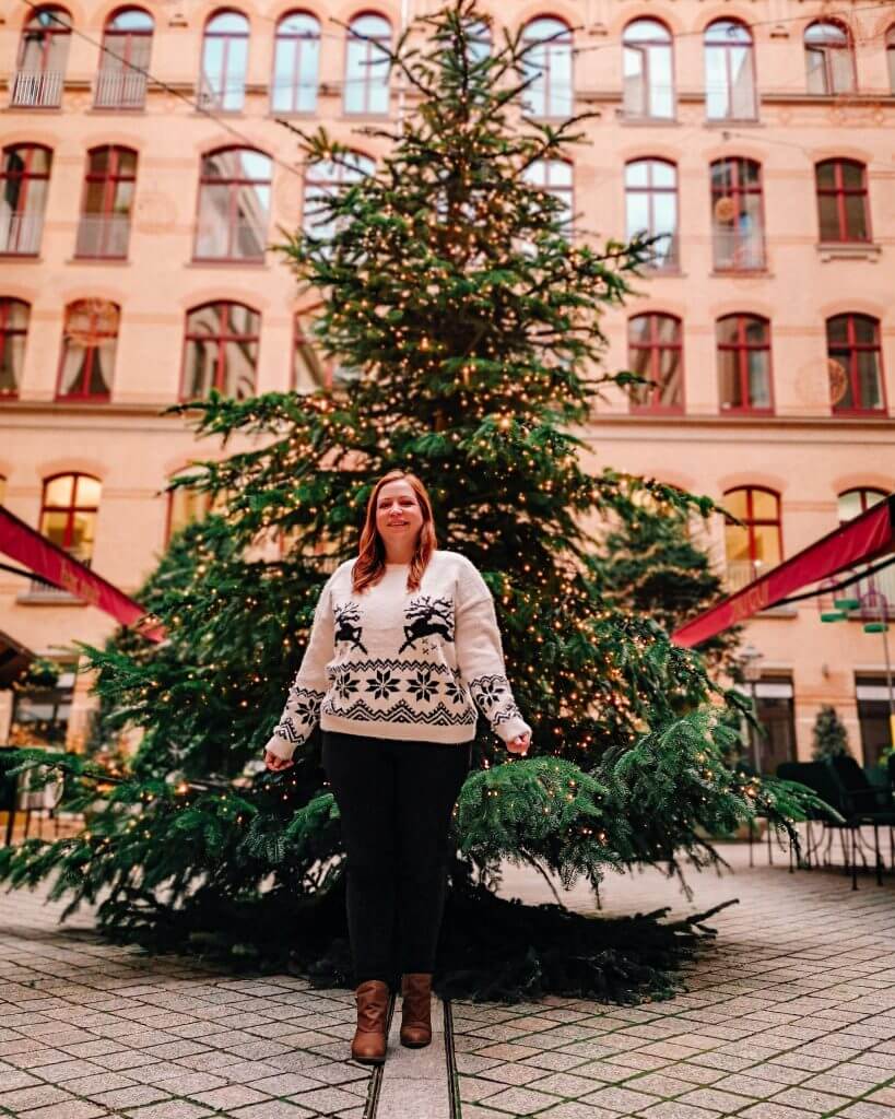 Girl standing in front of a Christmas tree wearing a Christmas jumper