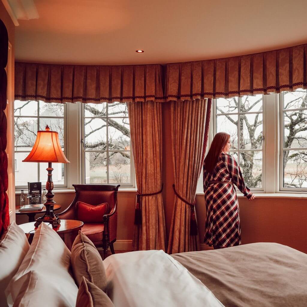 Woman in a checked dress in a luxury hotel room looking out of the window at the view