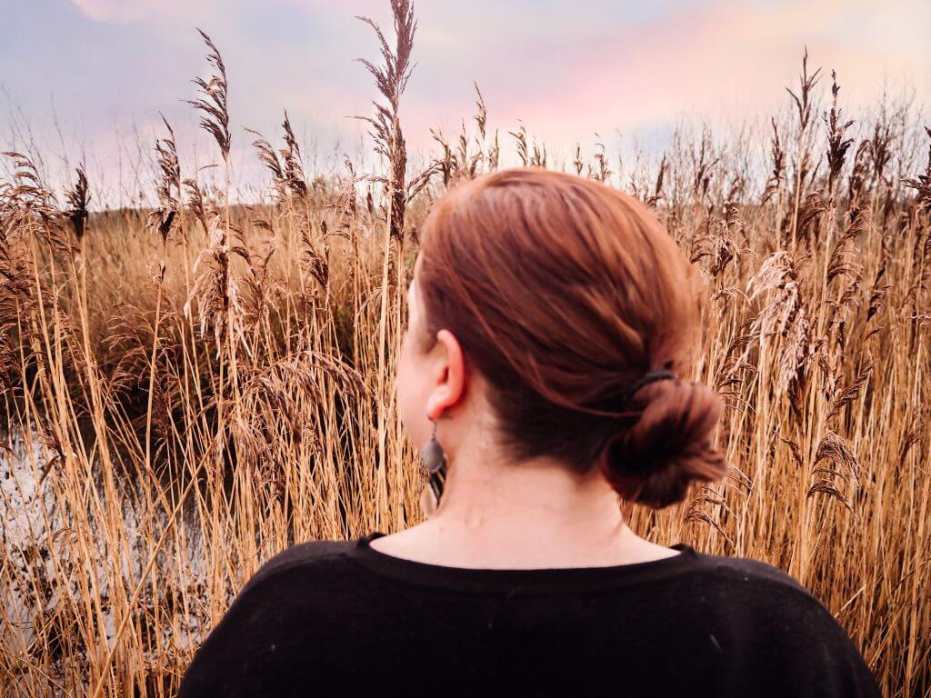 Woman wearing her red hair in a loose bun looking out over the reeds of Castle Hume Lough in Northern Ireland.