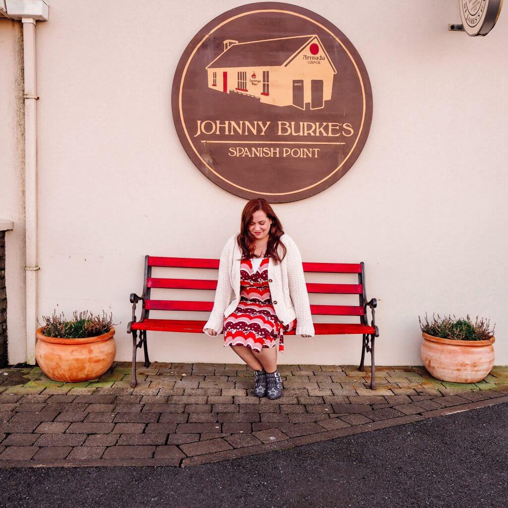 Woman sitting on a red bench outside Johnny Burke's Pub in County Clare Ireland