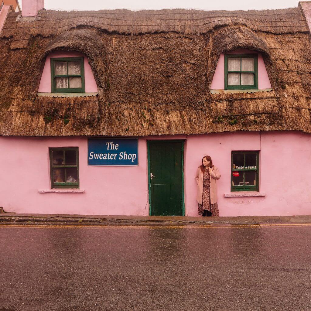 Irish woman in a pink coat resting against a pink thatch cottage in Doolin County Clare Ireland