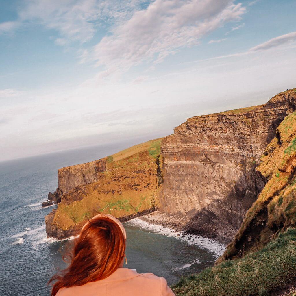 Woman with red hair watching the sunset from the Cliffs of Moher