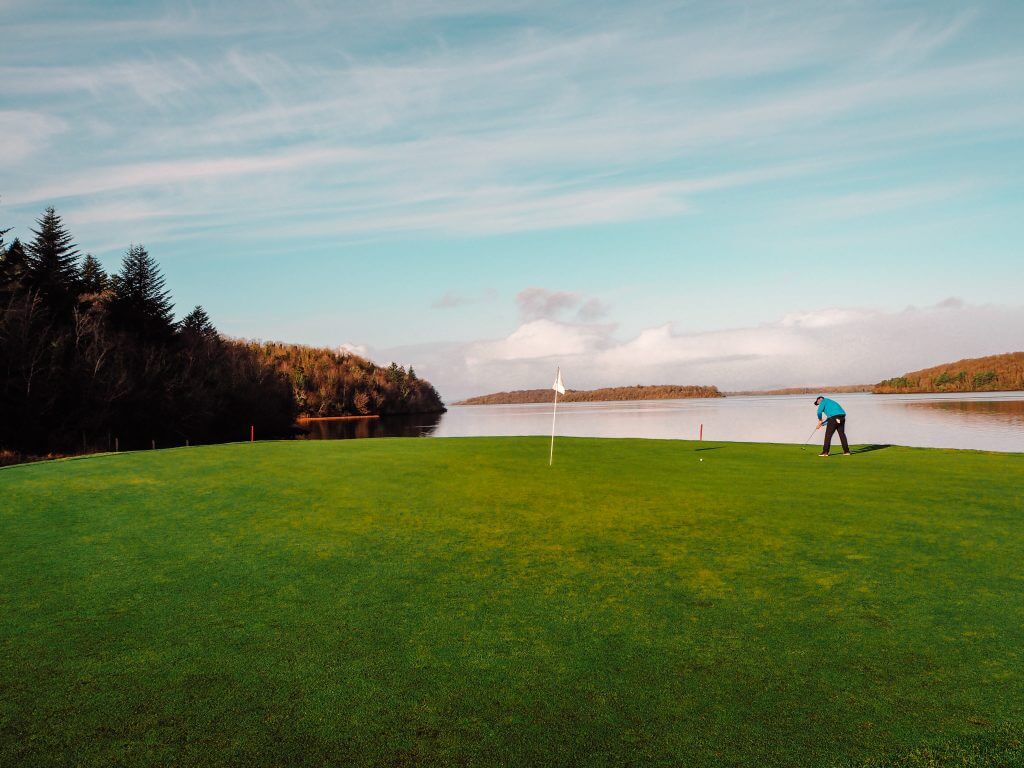 Male golfer in a blue top putting a ball on the signature hole in Lough Erne.
