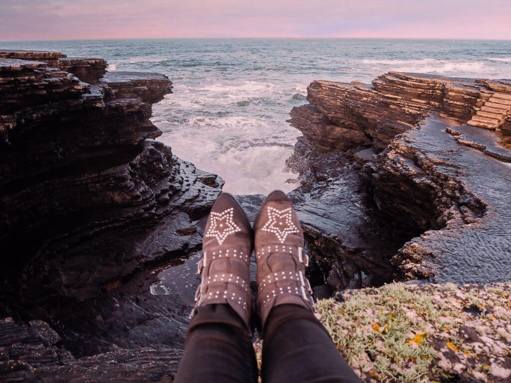 Legs wearing star studded boots hanging over a cliff edge on the Irish coast.