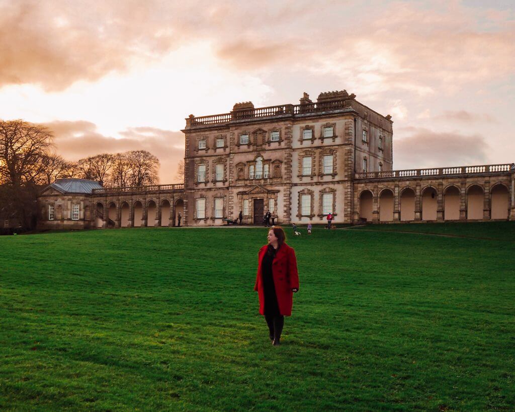 Women in a red coat standing in front of an 18th century Georgian house called Florence Court in Ireland.