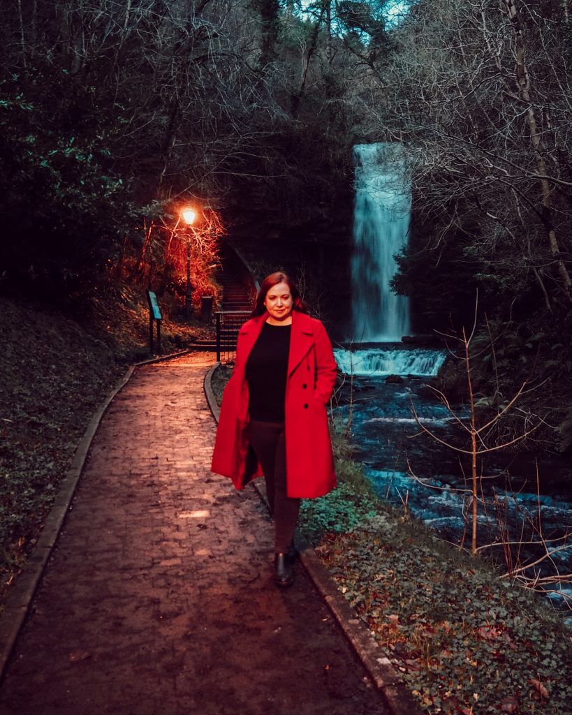 Woman in red coat standing in front of Glencar Waterfall in Leitrim Ireland