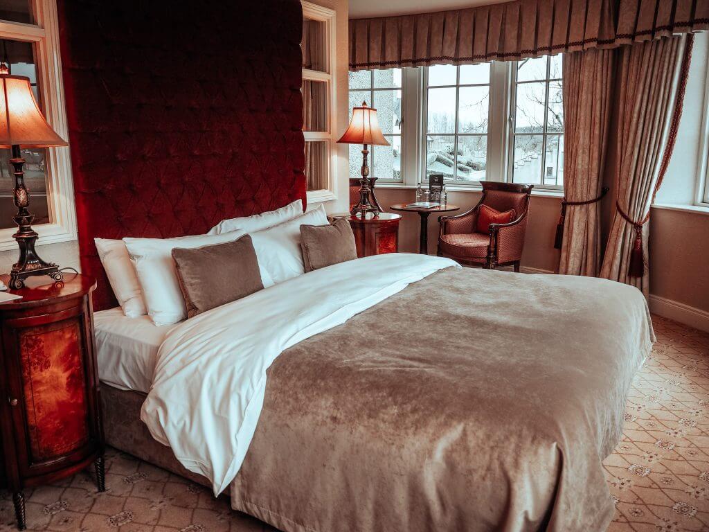 Large double bed with a red velvet bed head in a luxury hotel room at Lough Erne resort