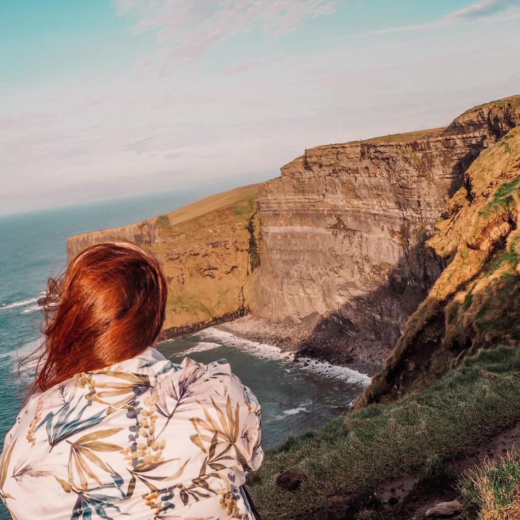 Woman looking over the cliff edge at the Cliffs of Moher Ireland