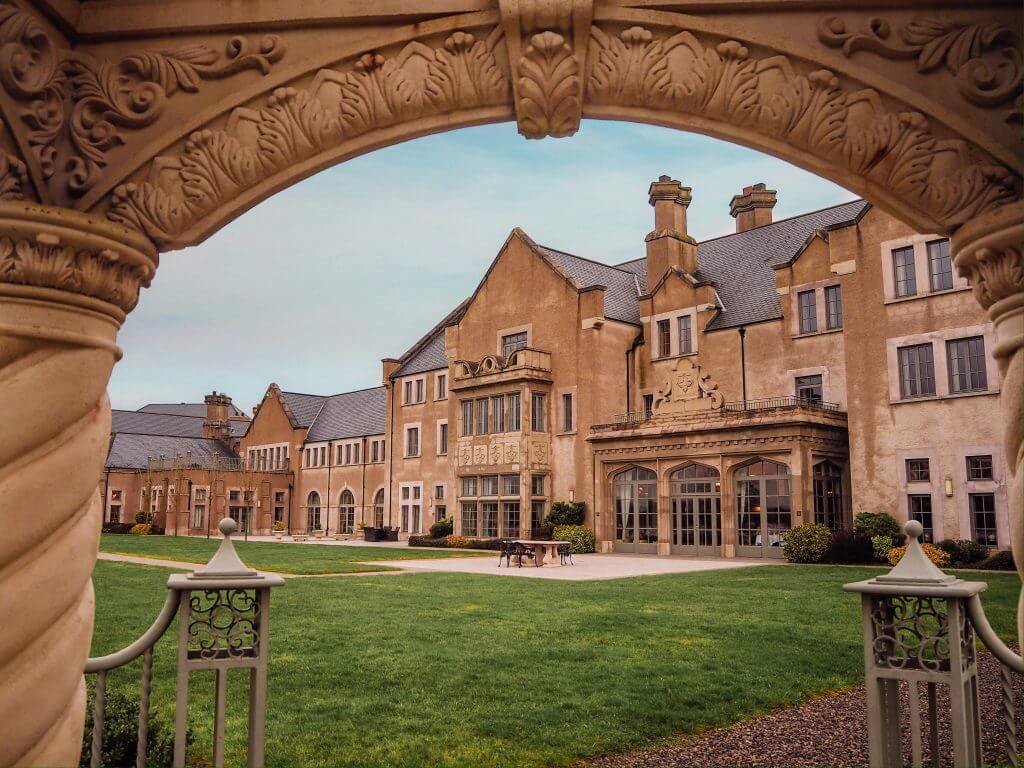 Main building of Lough Erne Hotel framed by the arch of the gazebo on the hotel grounds.