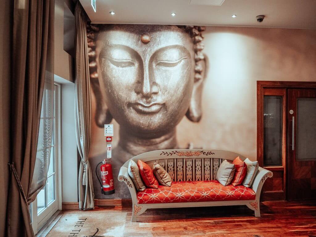 Thai spa at Lough Erne resort with a large mural of a buddha on the wall and a red couch to wait on.