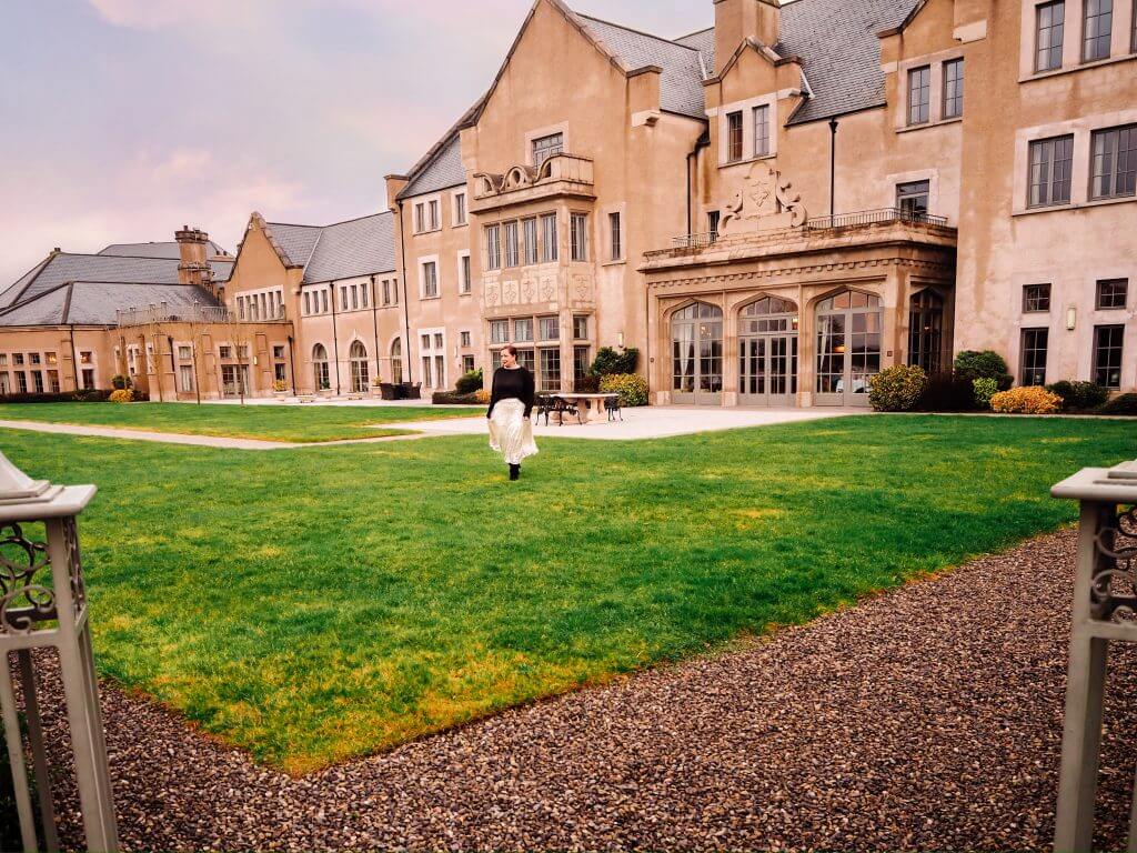 Woman with red hair ,wearing a silver sequin skirt walking in front of a country manor house hotel.