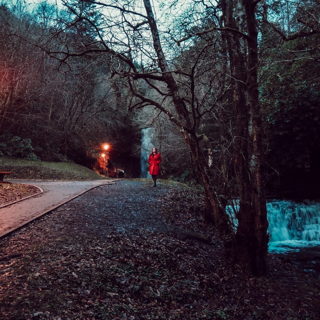 Woman in red coat standing in front of Glencar waterfall in Leitrim Ireland.