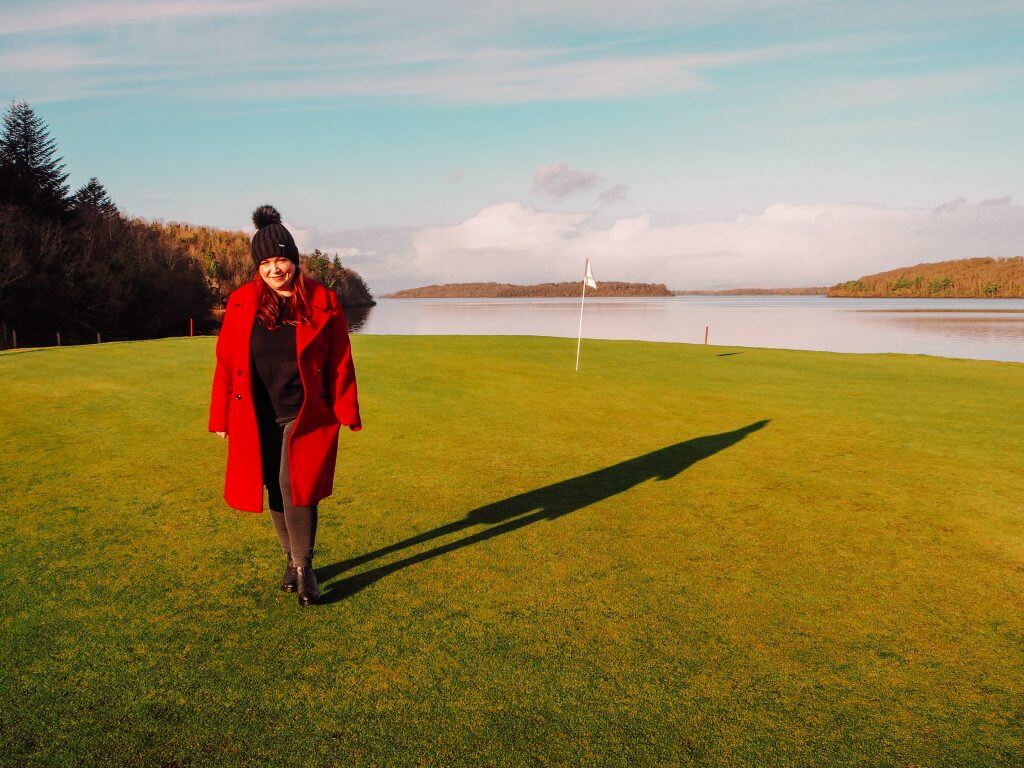 Woman in red coat walking on a golf course in Northern Ireland with a golf flag in the background.