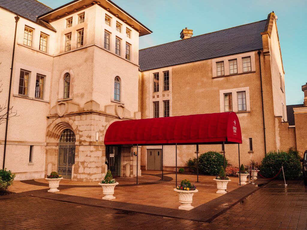 A hotel building with a large red awning over the entrance with potted plants around the entrance.