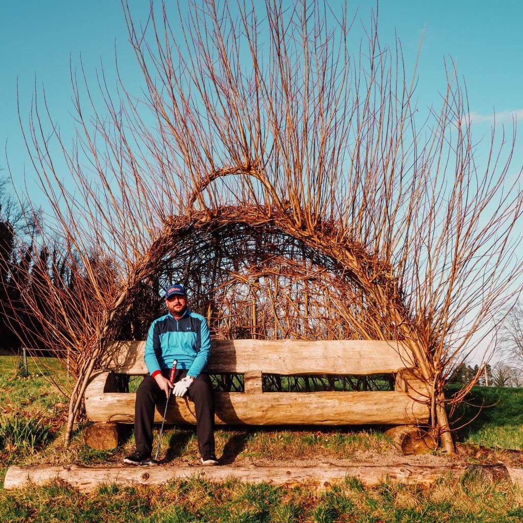 Male golfer in a blue top sitting on the love seat on the home straight on The Nick Faldo golf course in Ireland.