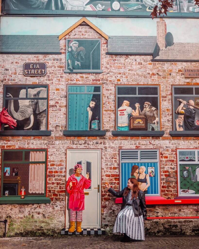Woman raising a glass of wine to a mural of a woman in Belfast's Cathedral Quarter. Best Instagram Spots Belfast