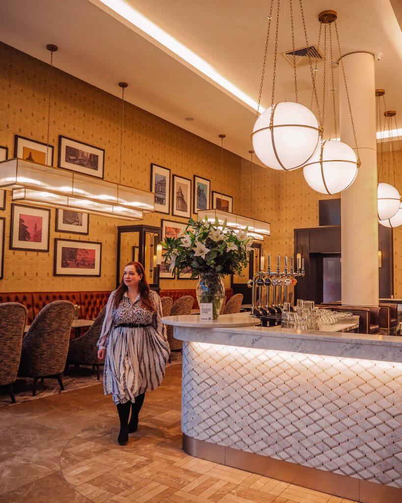 Woman in a white dress walking through the Grand Cafe in the Grand Central Hotel Belfast a beautiful Instagram Spot Belfast