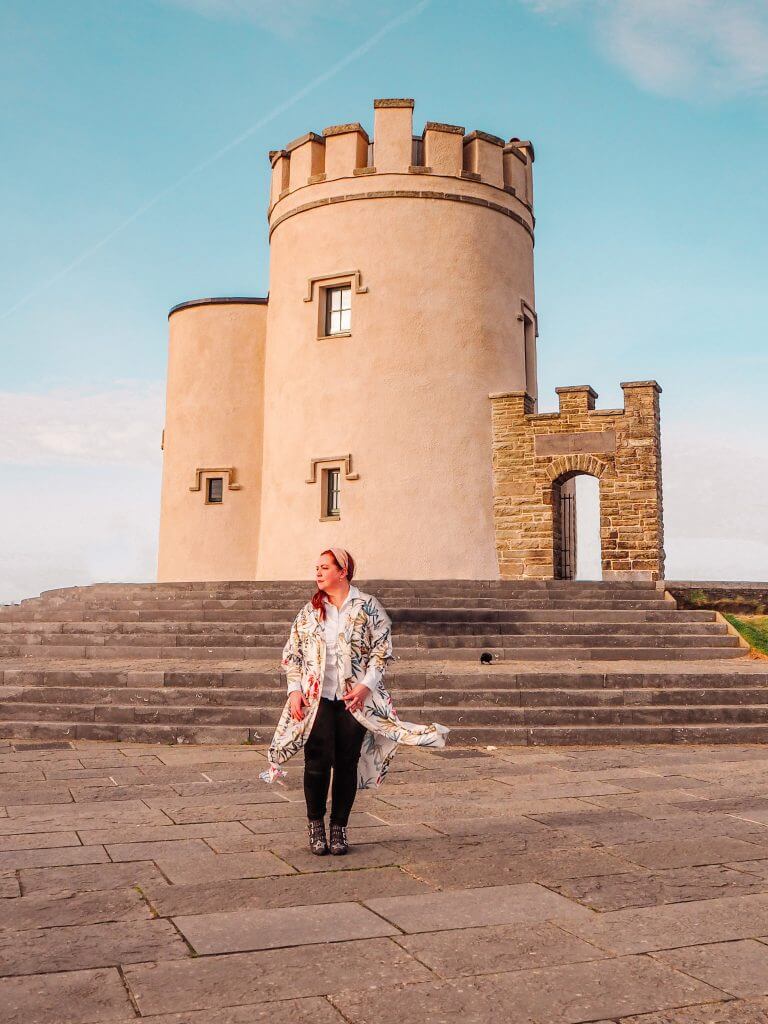 Woman in a long coat standing in front of O'Brien's Tower at the Cliffs of Moher
