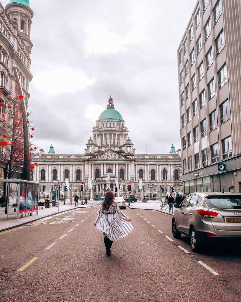 Woman wearing a white dress as she flicks her skirt in front of Belfast City Hall