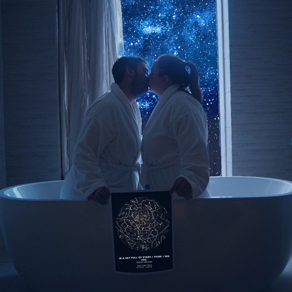 Couple kissing in a bath with a view of the night sky through the window