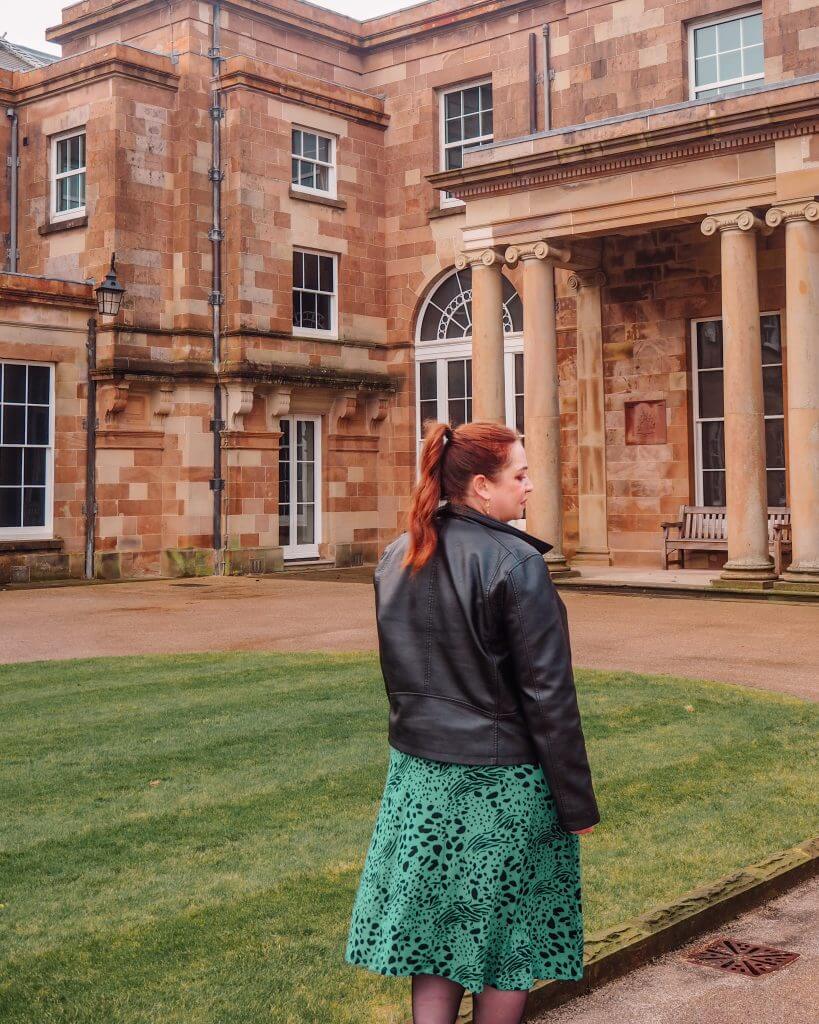 Woman in a green dress and black leather jacket walking the gardens of Hillsborough Castle and gardens in nortern ireland.