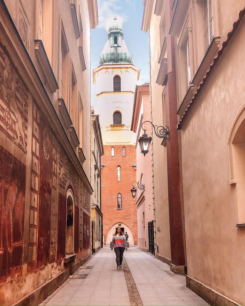 Woman wearing jeans and a stripe jumper walking down the alleyway of Bazylika Archikatedralna in Warsaw