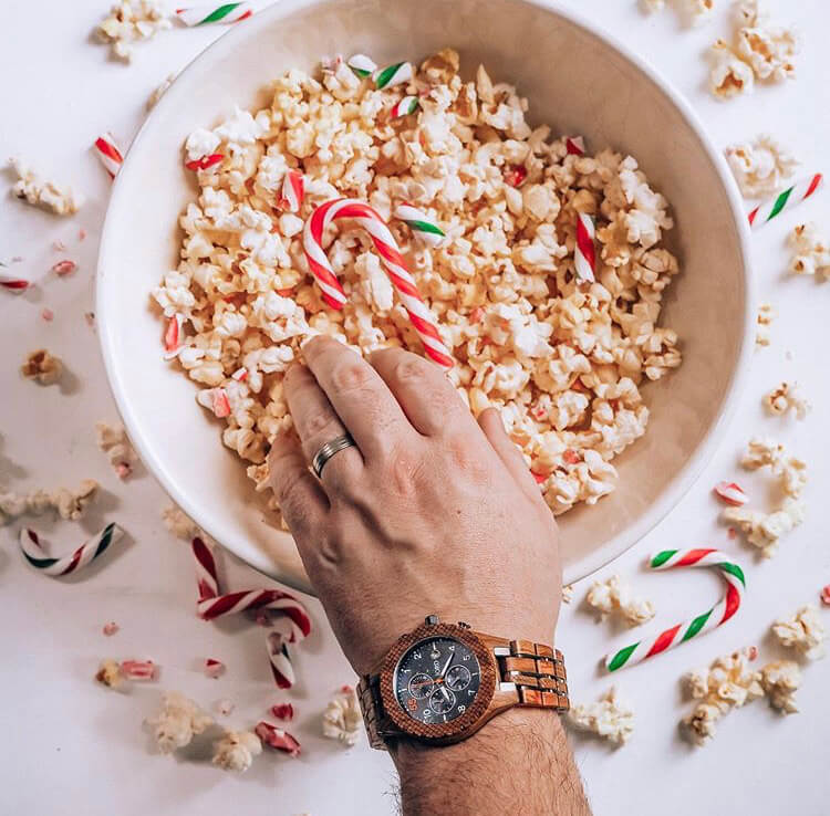 Man reaching his hand into a bowl of popcorn while wearing a Jord wood watch on his wrist working on a brand collaboration instagram