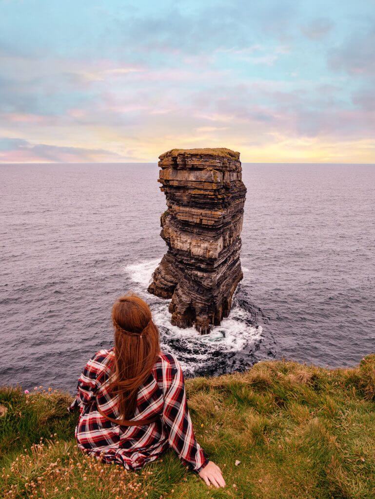 Woman in a tartan dress sitting at Downpatrick Head in county Mayo Ireland