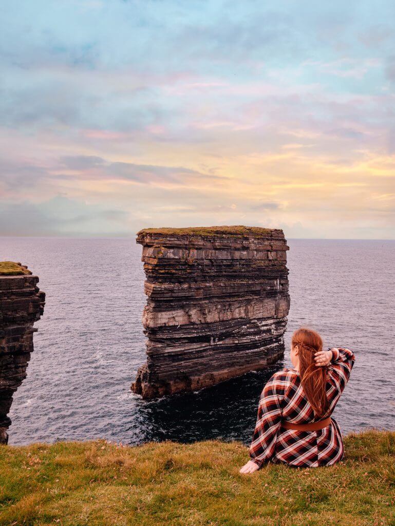 Woman sitting on a cliff edge at Downpatrick Head on the Wild Atlantic Way Ireland