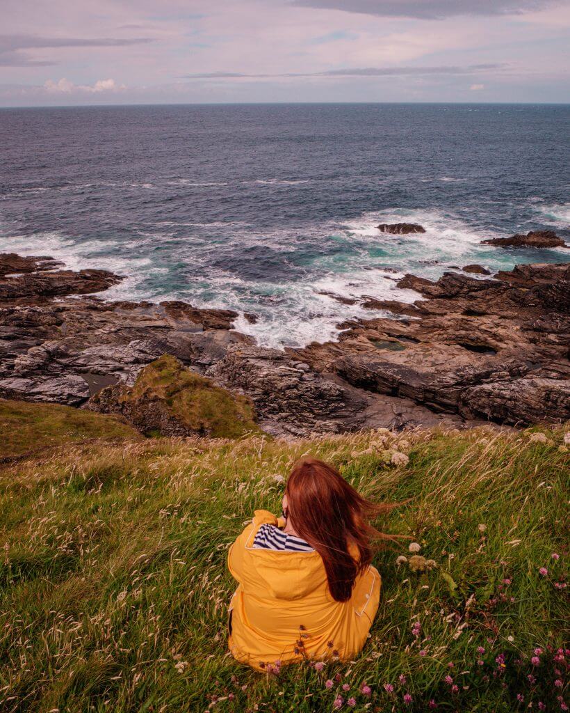 Woman in a yellow raincoat overlooking the cliffs at Malin Head in Donegal