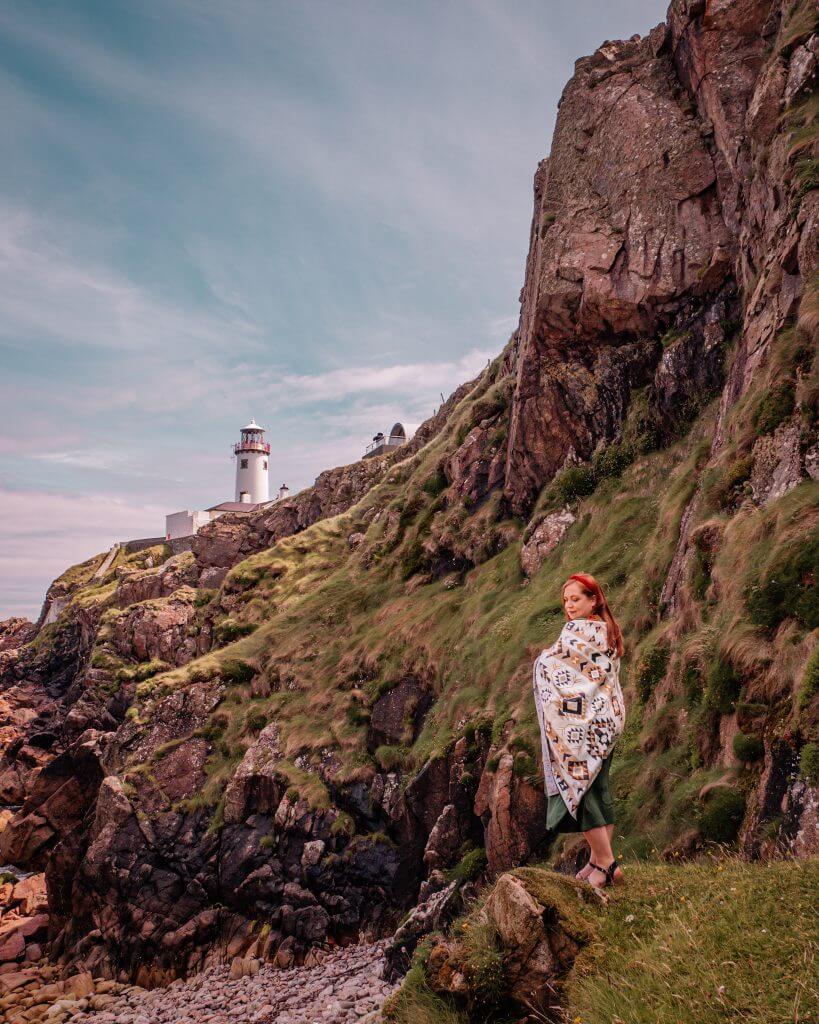 Irish woman with red hair standing on rocks at Fanad Head Lighthouse in County Donegal Ireland
