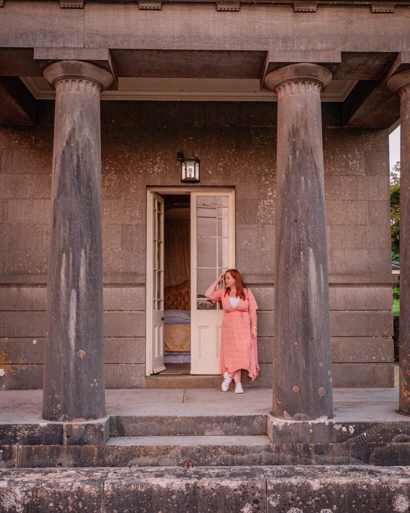 Woman in a red dress standing outside her bedroom at Loughcrew Lodge a 200 year old gatehouse in Ireland