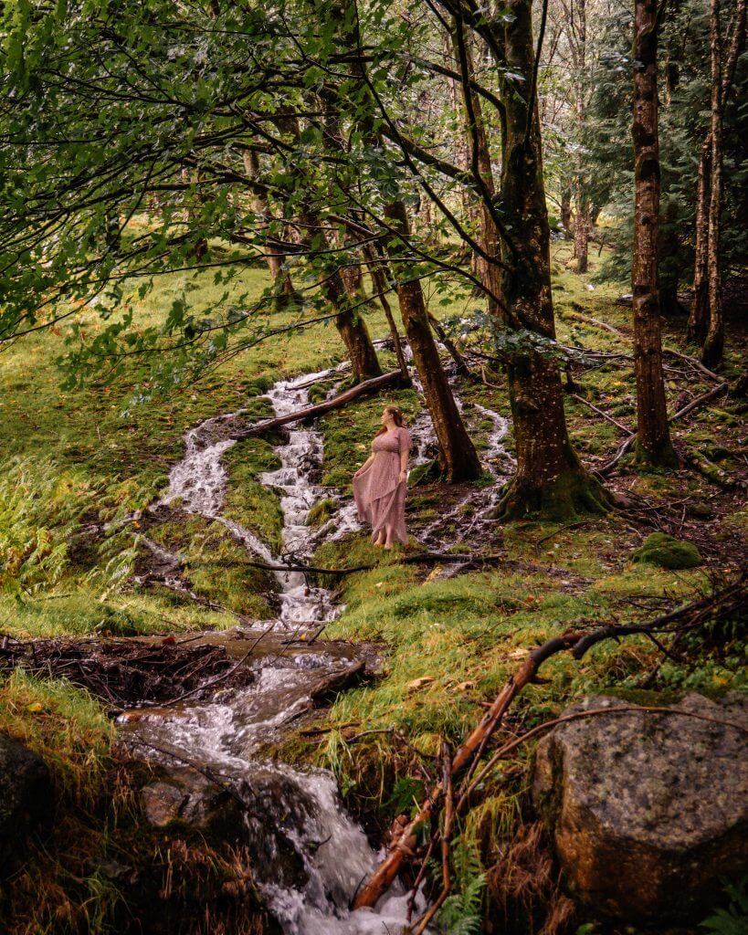 Woman in a purple dress standing at a waterfall in Glendalough Wicklow on her staycation ireland